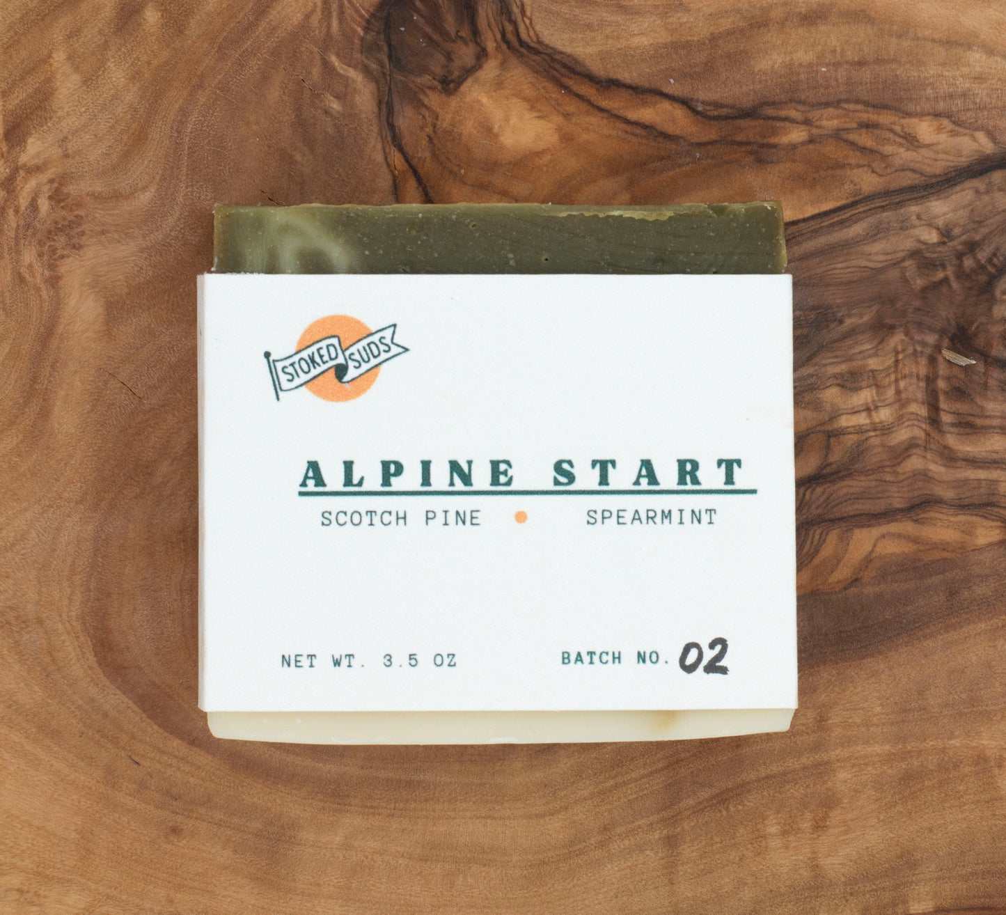 A bar of soap with 'Alpine Start' text and 'Scotch Pine - Spearmint' label, placed on a wooden surface.