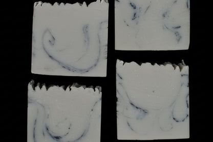 Four square soap bars with a marbled pattern on a dark background