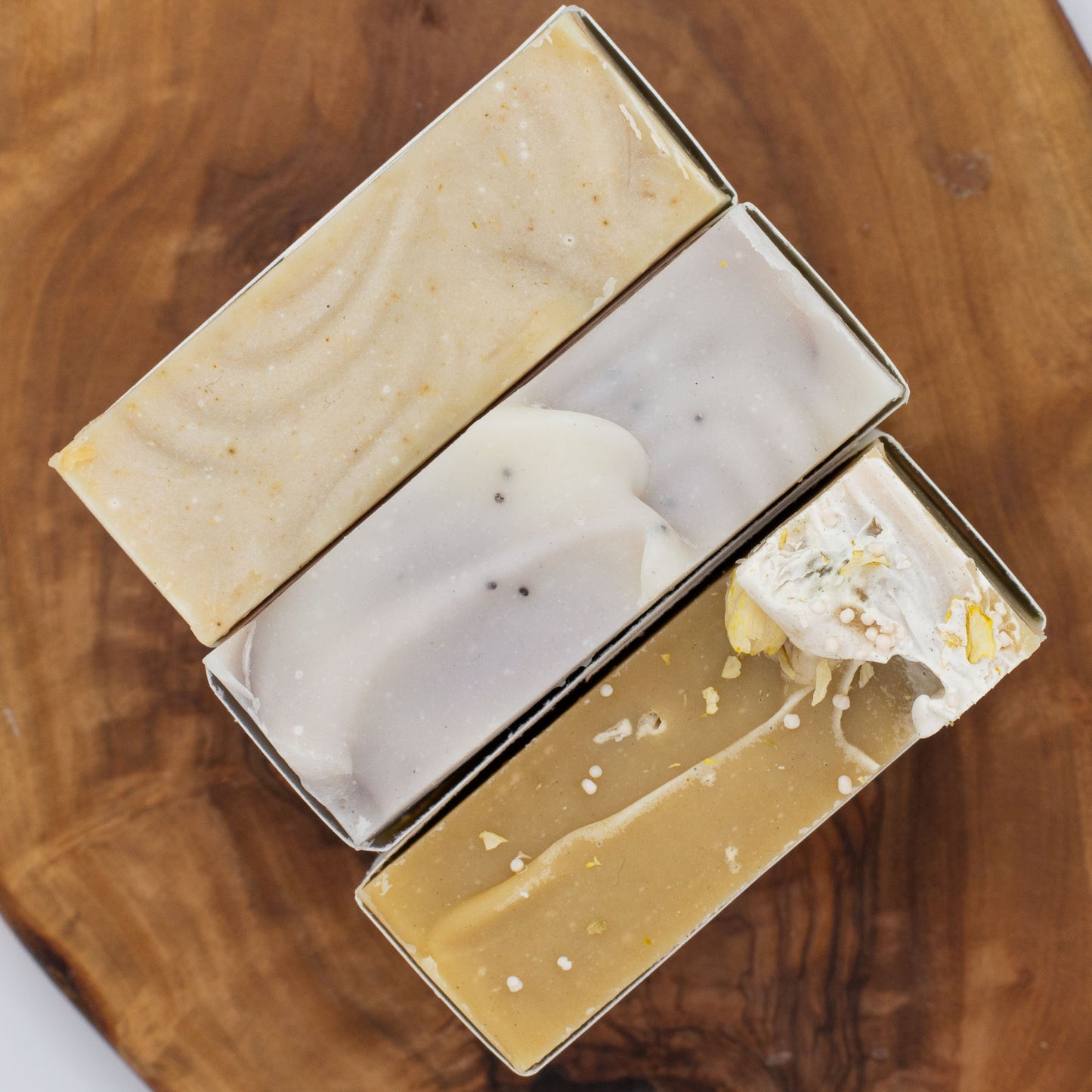 Three bars of soap on a wooden surface with different textured soap tops