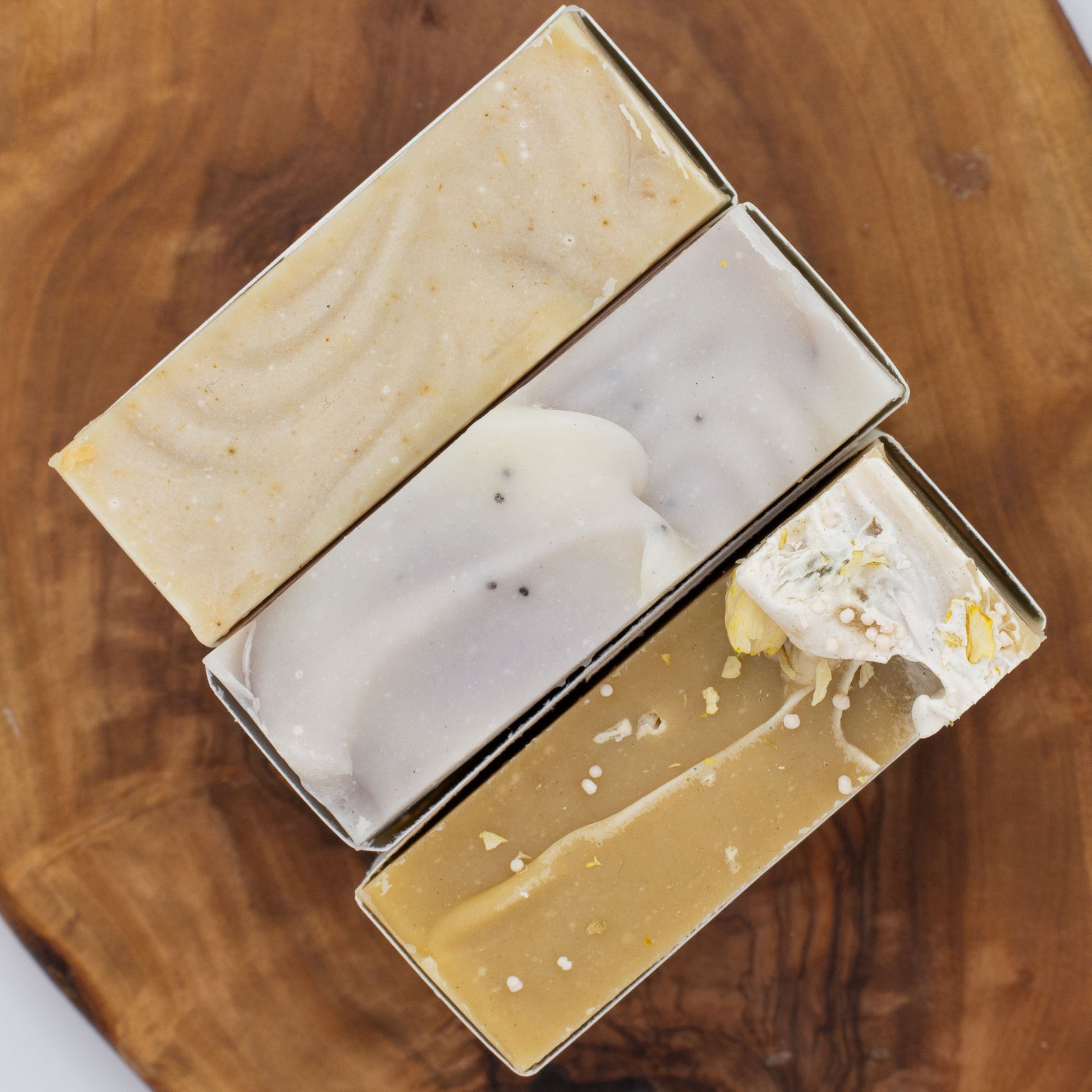 Three bars of soap on a wooden surface with different textured soap tops